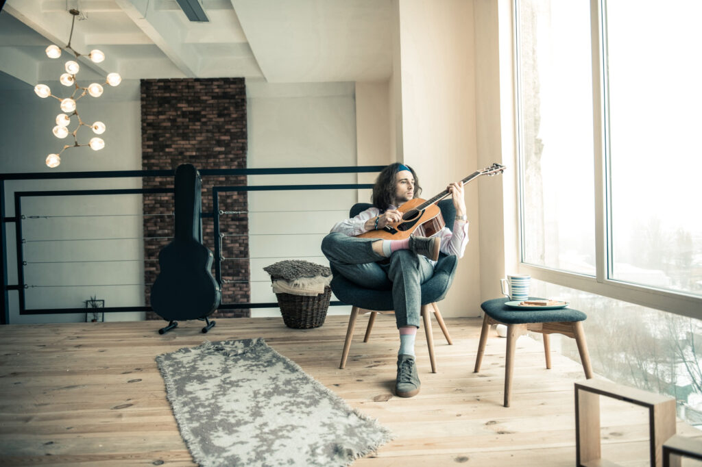 twanging-guitar-melancholic-stylish-musician-being-alone-home-sitting-bright-room-with-his-musical-instrument